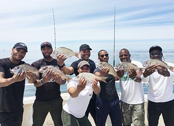 On a sunny day, a group of 6 men and 1 woman each hold up the scup/porgy they caught.
