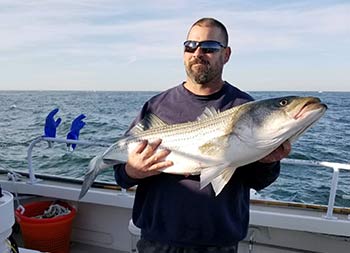 A man wearing sunglasses proudly holds up the fish  he caught.