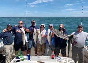 A group of 7 men each hold up the fish they caught and smile.