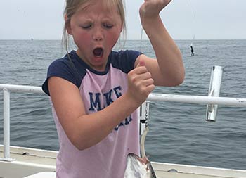 A young girl has a look of excitement and awe as she looks at the fish she caught.