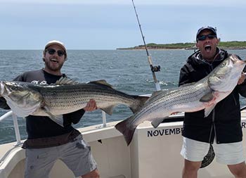 With the lighthouse obscured in the background, two men excitedly hold up the fish they each caught.