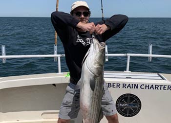 A man uses two hands to hold up the large striped bass he caught.