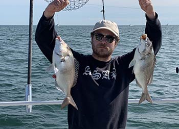 A man wearing sunglasses proudly holds up the two fish he caught.