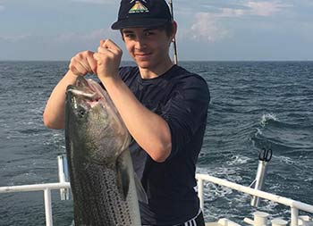 A young man proudly holds up the striped bass he caught.