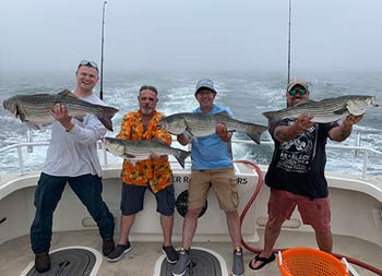 On an foggy day, 4 men smile big and hold up the fish they each caught.