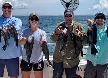 A man with his father and two young adult children, a boy and girl, each hold up sea bass and smile for the camera.