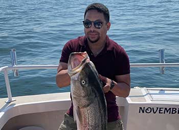 A man uses two hands to hold up the large striped bass he caught.