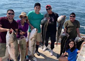 A family of six smile for the camera as they hold up 7 striped bass.