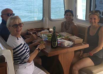 Four women and men sit inside the boat in the galley for lunch and smile for the camera.