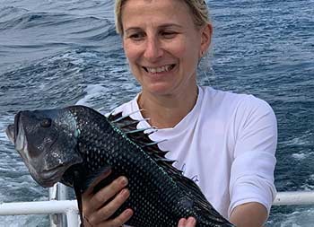 A woman looks at the sea bass she caught as she holds it up for the camera.