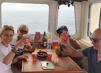 Four women and men sit inside the boat in the galley and toast champagne for the camera.