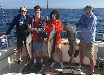 Two parents and their two young adult sons smile and hold up 3 striped bass.