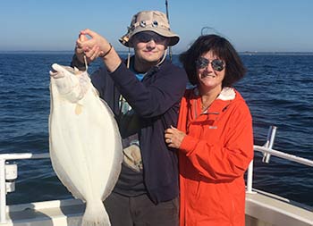 A mother stands next to her son and smiles as he holds up a large fluke .