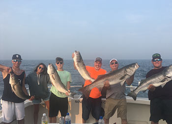 A group of six men and women each hold up striped bass for the camera.