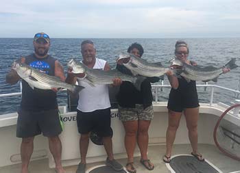 Two men and two women smile and each hold up striped bass.