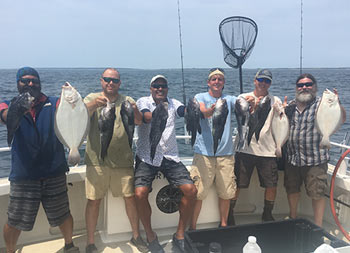 A group of 6 men smile and hold up a mis of sea bass and fluke.