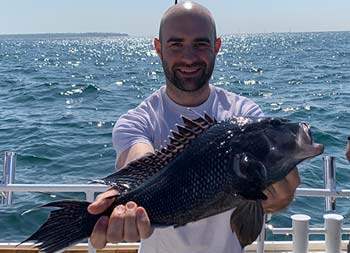 With the blue sky and ocean behind him, a man smiles for a close up holding sea bass.