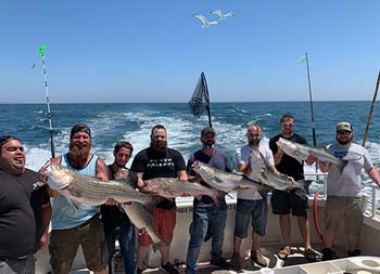 Eight men stand side by side and hold up the striped bass they caught.