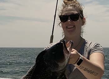 A woman holds a sea bass that she just caught.