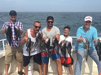 Four men and a young boy each hold up two sea bass, one in each hand.