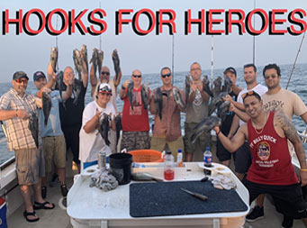 A large group of men smiling and eah holding up the sea bass they caught.