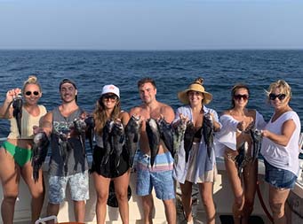 A group of 7 men and women hold up 2 sea bass each.