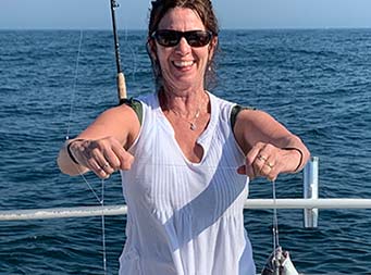On a sunny blue sky day, a woman put on a toothy smile and holds up sea bass in each hand, still on the line.