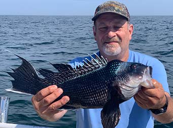 Close up of a man, looking at his sea bass as he holds it up for the camera.