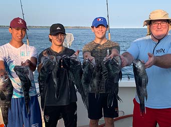 Around sunset with shadows being cast, a man and 3 young men each hold up 2 sea bass.