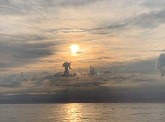 View of the vast oncea and soft clouds in the sky as the sun goes down and approaches the horizon, leaving the sky a pale blue and orange.