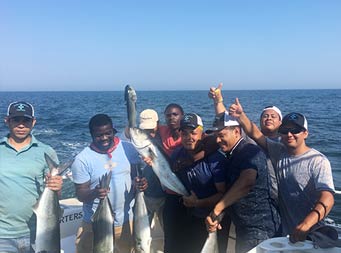 Eight men on the boat holding up their carch and giving thumbs up for the camera .