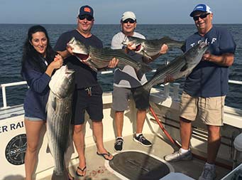 A woman and three men each smile and hold up striped bass.