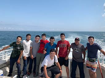 On a sunny blue sky day, nine men stand together for the camer and smile.
