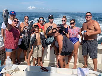 A group of 9 adult men and woman and a young boy cheerfully pose for the camera and hold up the fish they caught.