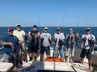 On a clear blue sunny day, seven men each hold up 2 bass and smile for the camera.