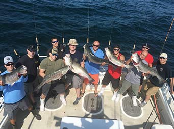 View from a top the boat looking down at nine men smiling and holding up striped bass.