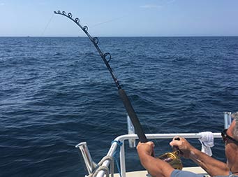 View from behind a man with his rod and line in the water reeling something in