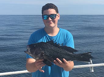 A young man holds up a sea bass and smiles.