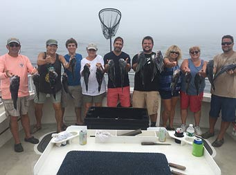 On a cloudy, rainy day, 9 men and women each hold up 2 sea bass.