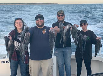 With the sun just about set, two men and two women each hold up two sea bass.