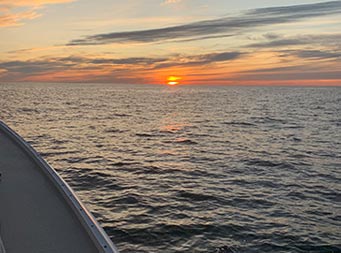 View from the deck of the boat of the sun setting in the distance on the horizon.