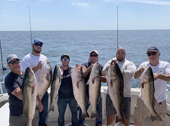 Six men ranging in age, each hold up the striped bass they caught.