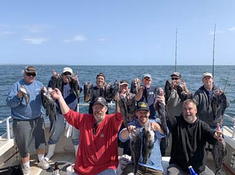 A group of 10 men sit and stand posing for the camera, all holding up sea bass.