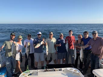 Ten men and women stand together and hold up some bluefish.