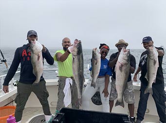 Four men and one woman smile and each hold up striped bass.
