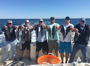 Six men ranging in age hold up the sea bass they caught.