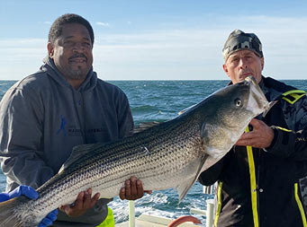 Three men on the boat on the water each hold up 2 sea bass and smile.
