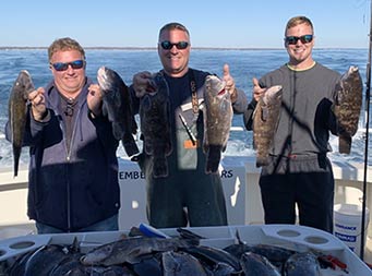 On a sunny, brisk day, 3 men each wearing sunglasses hold up 2 sea bass each.